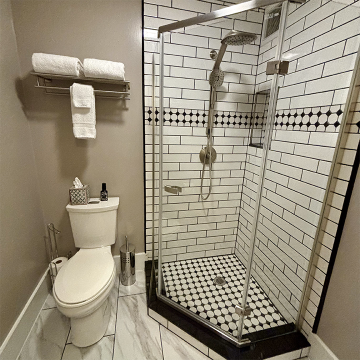 Picture of recently remodeled Charles Suite bathroom and shower, showing clear glass and tile shower enclosure, multi-sprayer shower head, and new tile floor.