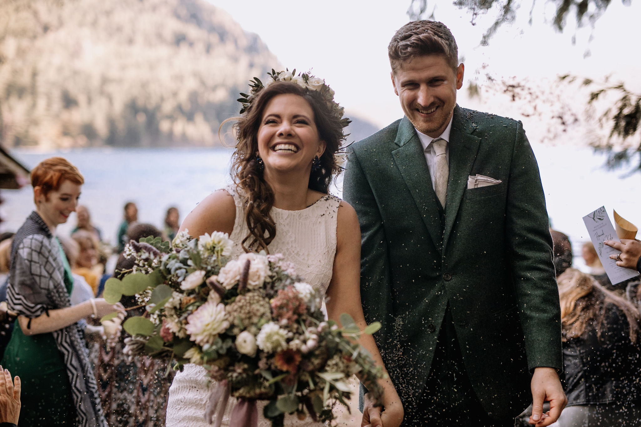 Couple getting married at Lake Crescent, WA Man and woman in wedding attire with guests sitting behind them and Lake Crescent, WA in the background