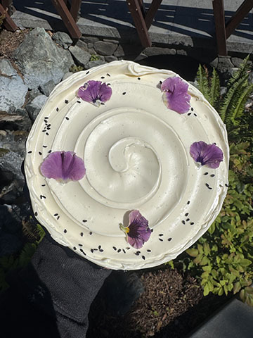 Bautiful white icing cake with purple flower petals on top, in a forest background